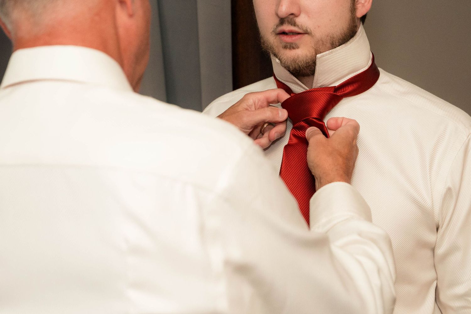 Man in white shirt getting red tie adjusted by another person, perfect for wedding preparation concepts.