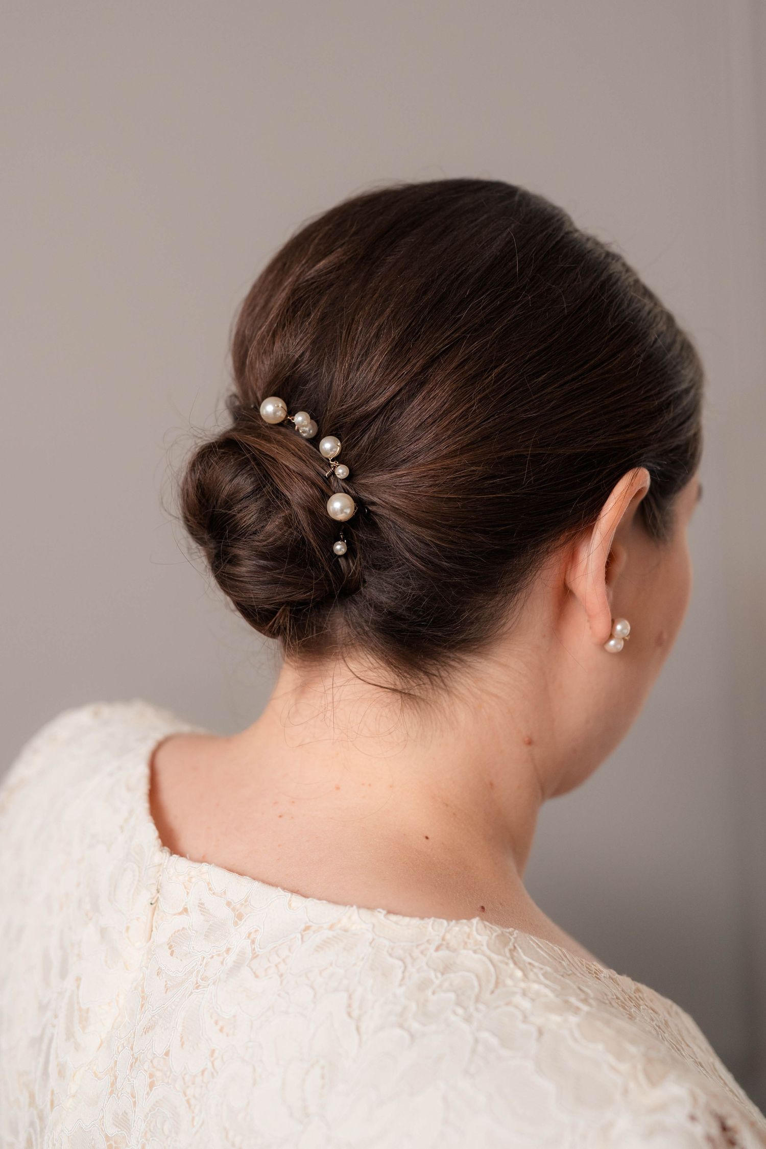Bride's elegant low bun hairstyle adorned with pearl hair pins and pearl earring.