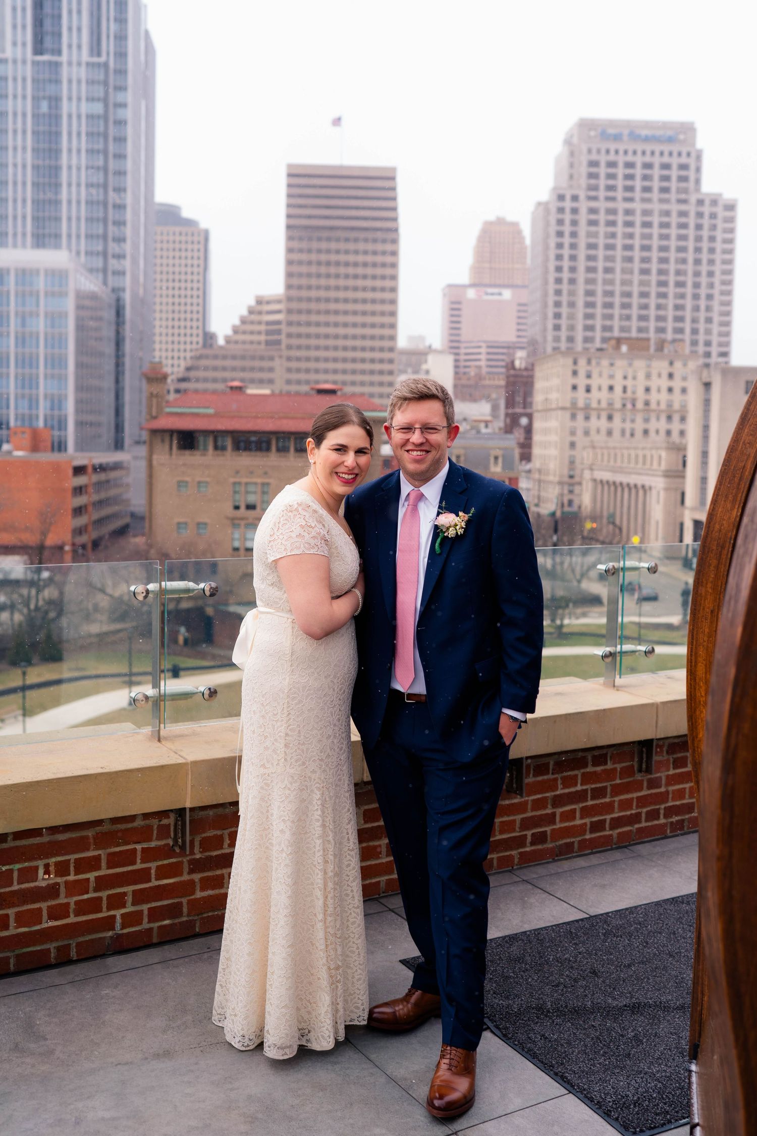 Elegant bride and groom posing together on rooftop venue with impressive city skyline background.
