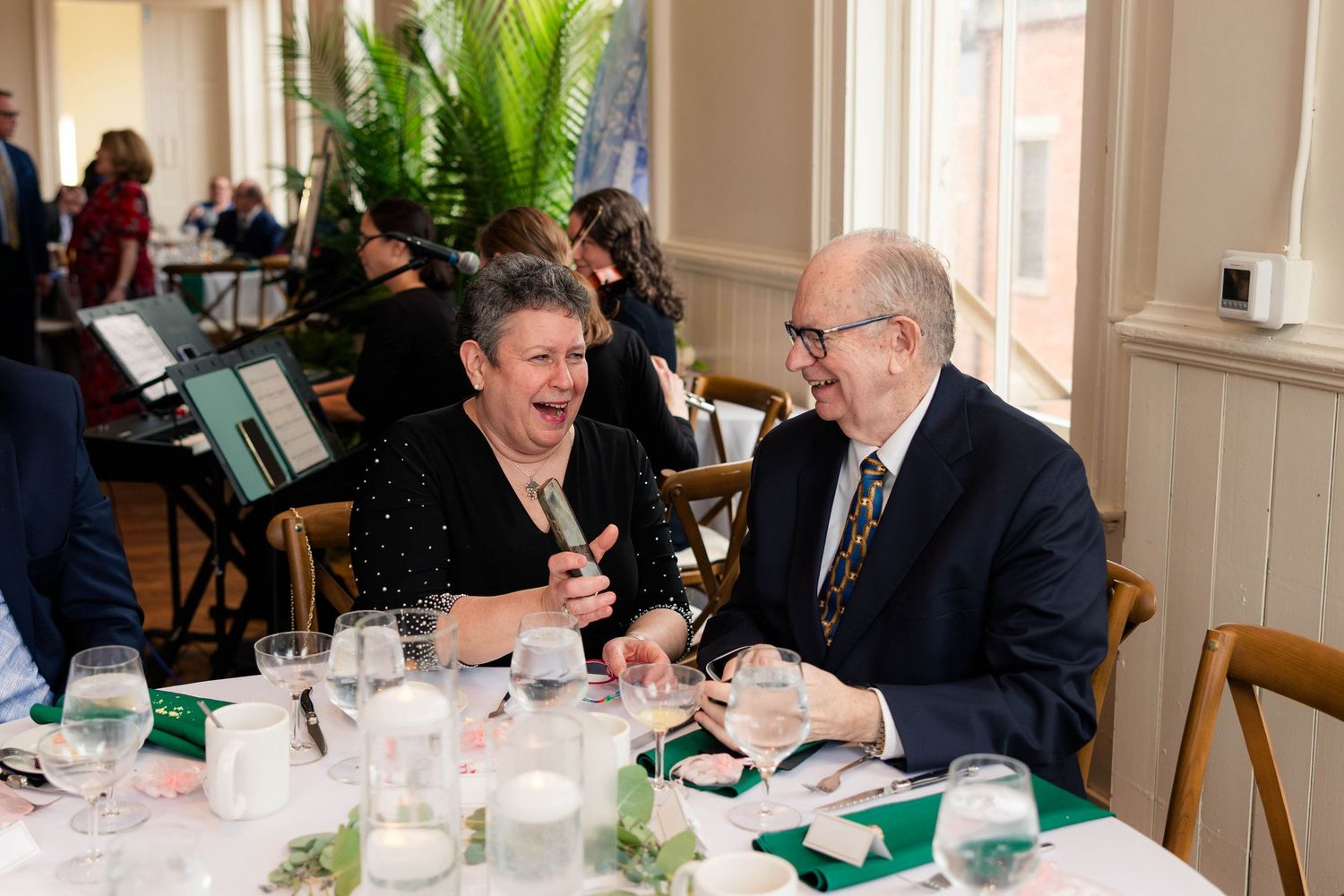 Two guests laughing joyfully together at a formal dinner event.