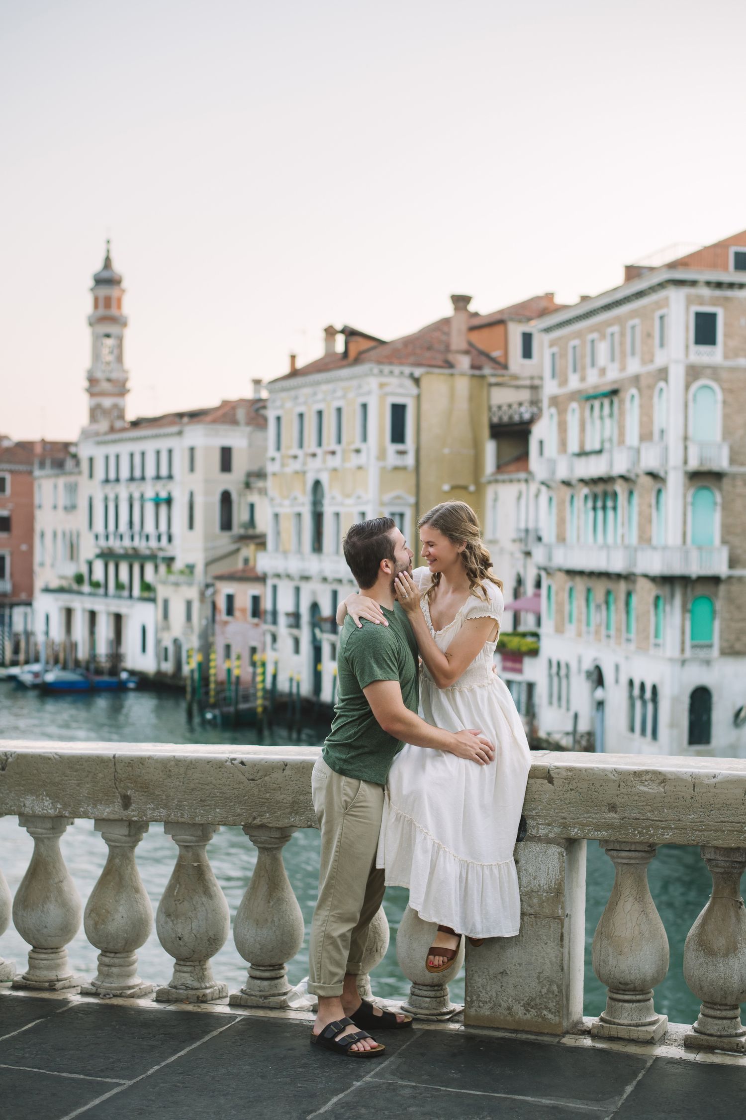 Romantic couple embracing on Rialto Bridge overlooking the Grand Canal at sunrise in Venice Italy.