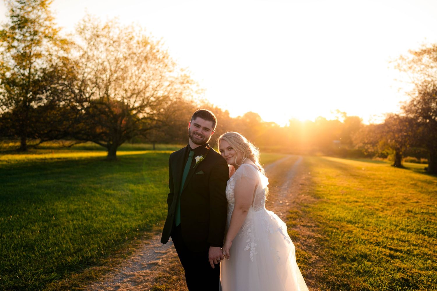 A bride and groom hold hands at golden hour sunset in a lush green park, radiating romance on their wedding day.