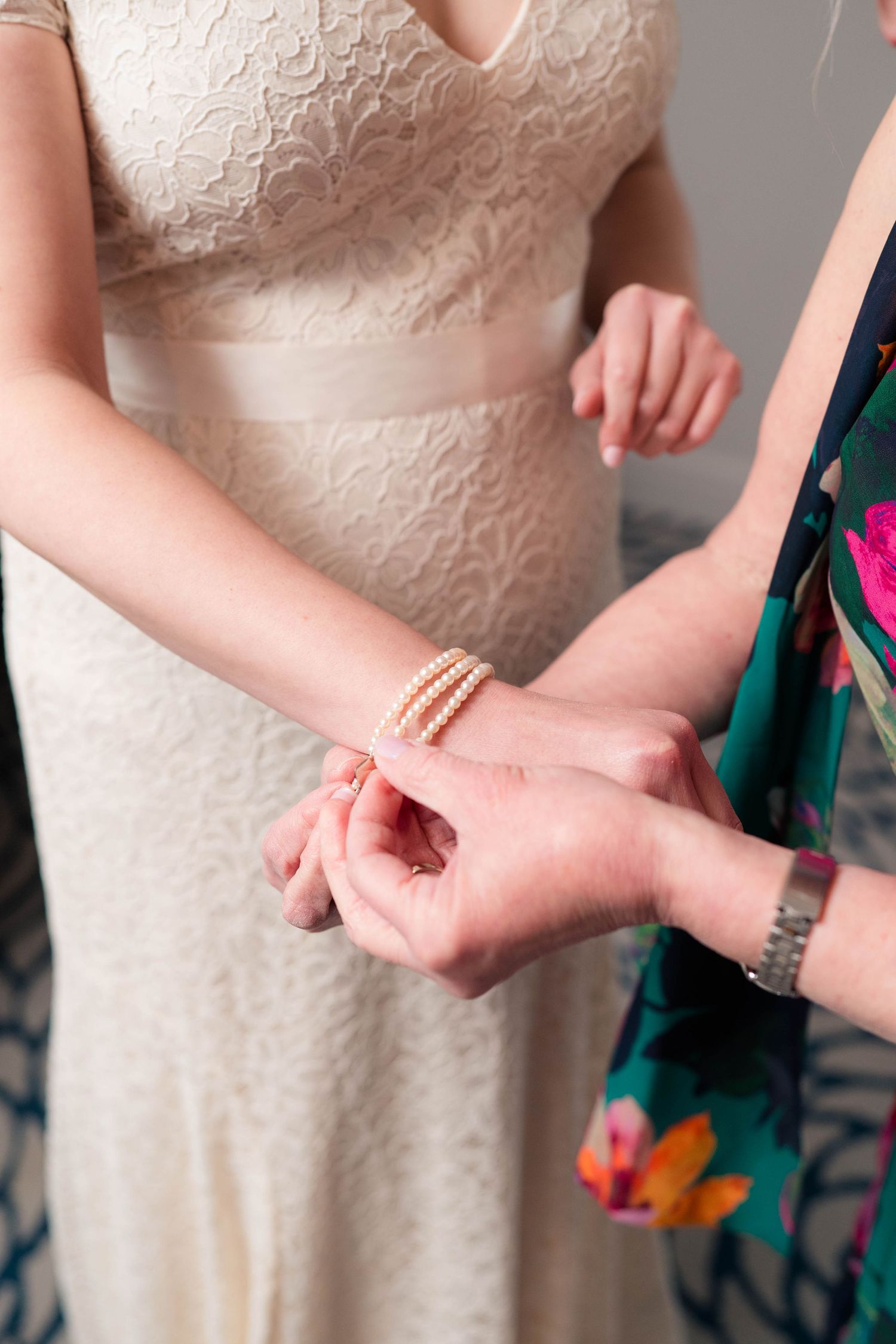 Mother clasps a triple-strand pearl bracelet onto bride's wrist before wedding.