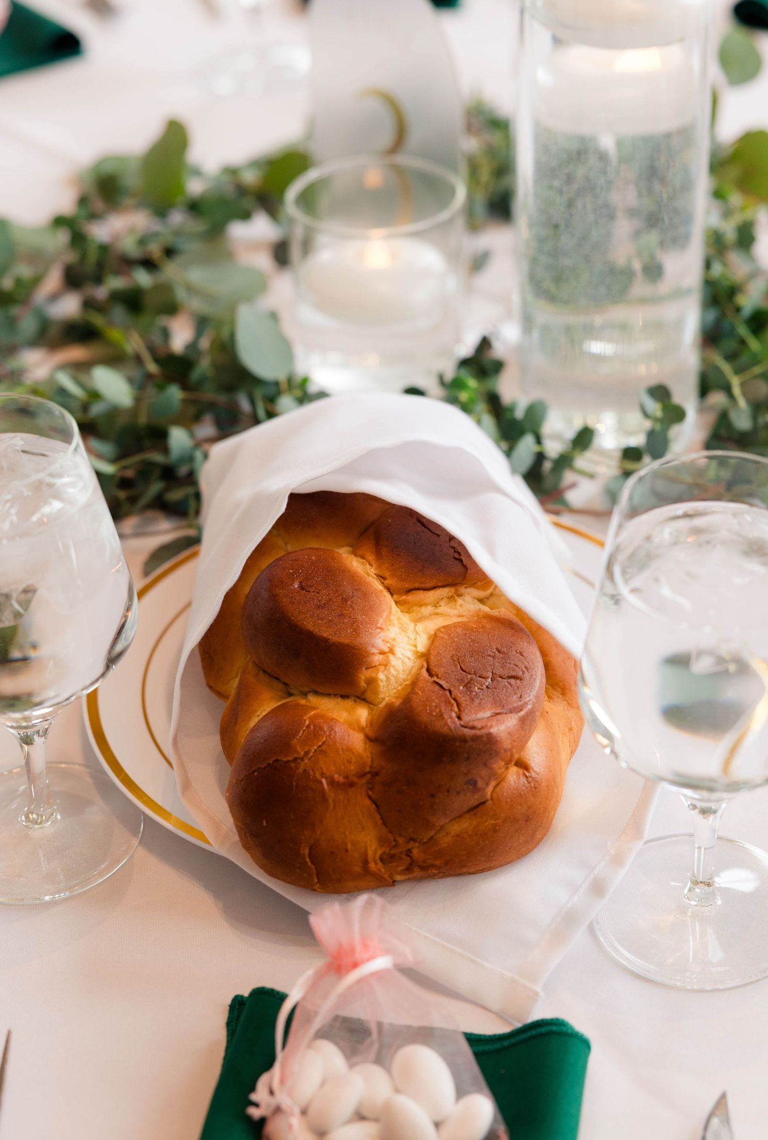 Traditional challah bread wrapped in white cloth displayed as a centerpiece on a wedding reception table.