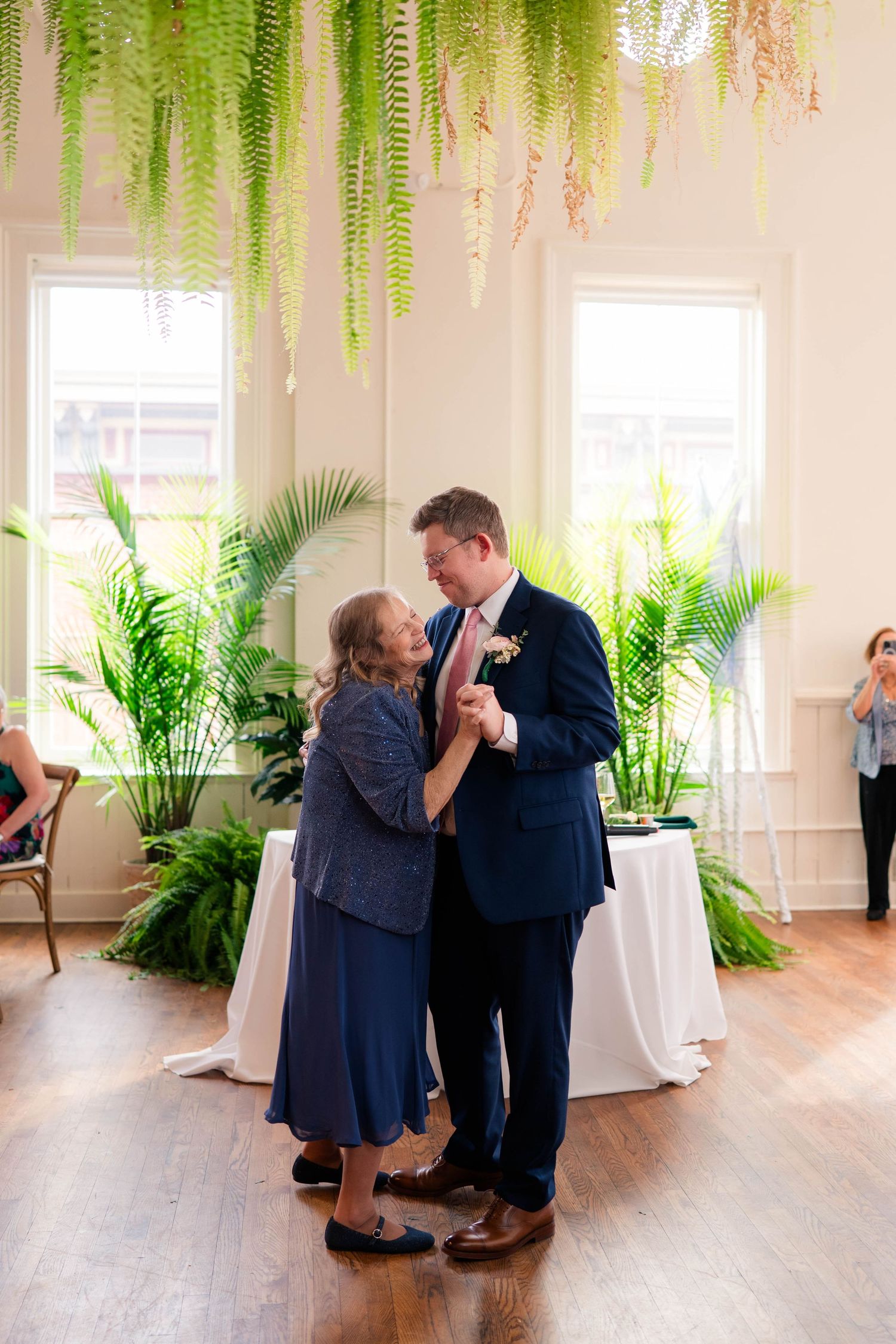 Groom dancing with mother at wedding reception surrounded by lush tropical greenery.
