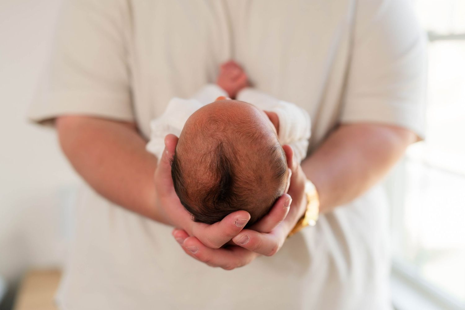 Close-up of a parent gently cradling a newborn baby's head in their hands, showcasing new life and parental love.