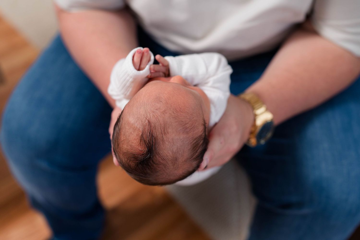 Adult holding a swaddled newborn baby in their arms, wearing jeans and a gold watch.