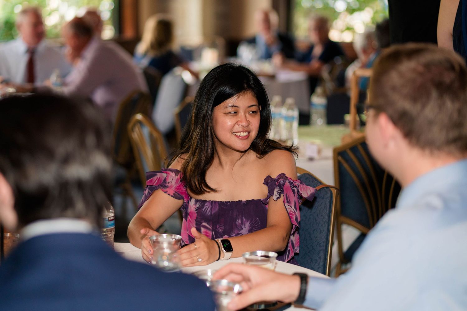 Young woman in floral off-shoulder top smiling at a formal banquet event.