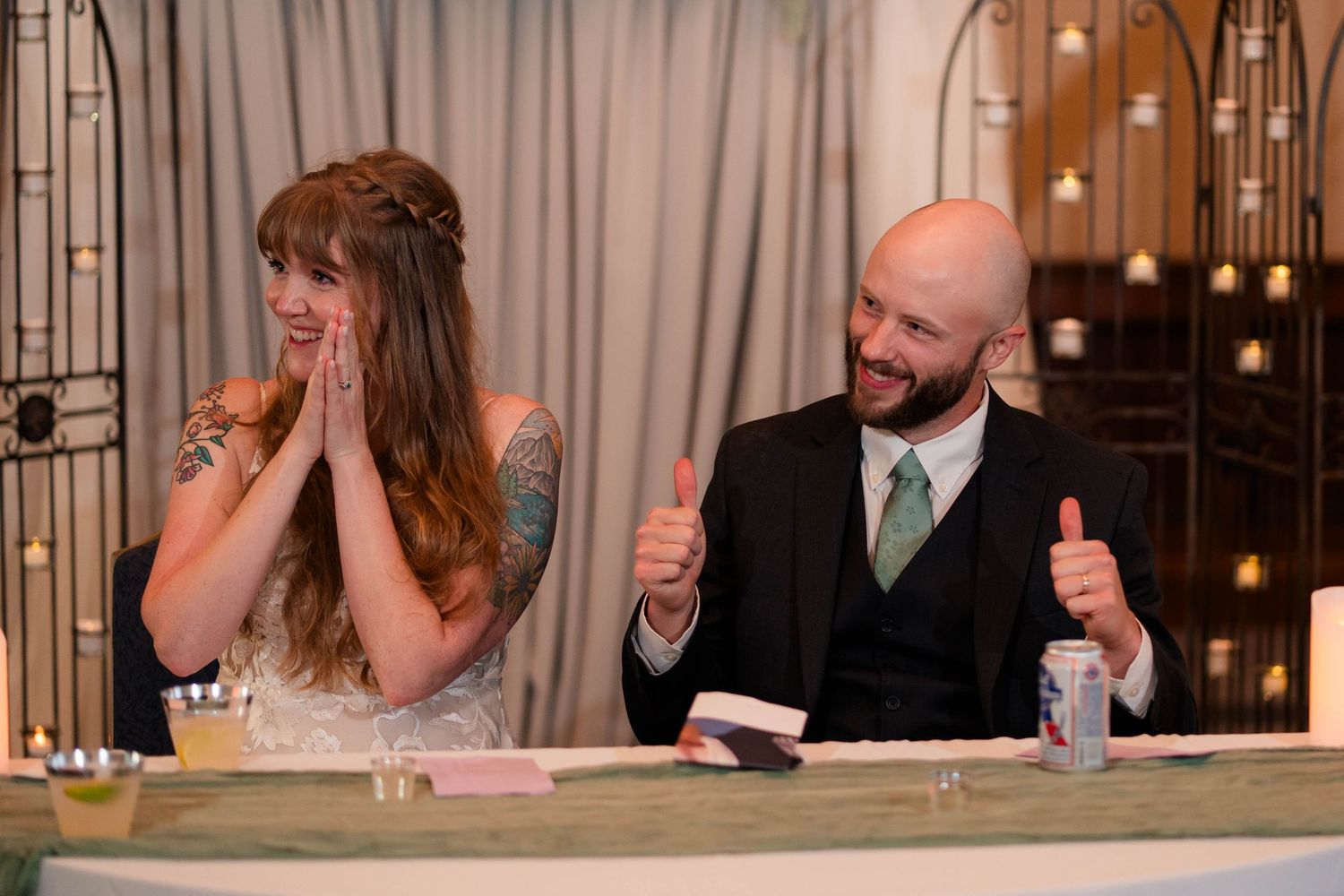 Bride and groom reacting with joy at wedding reception sweetheart table.