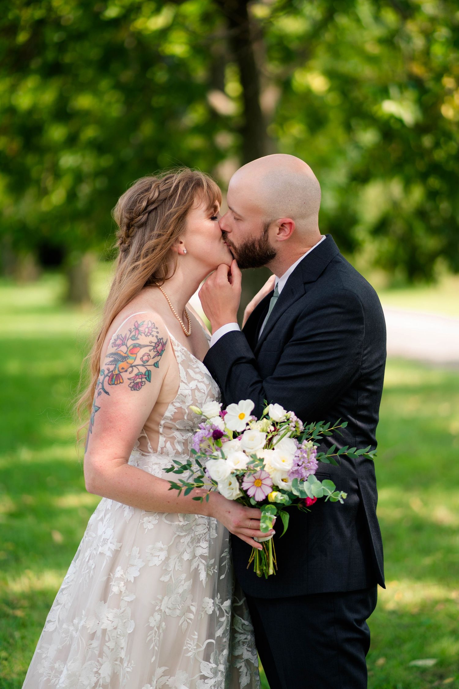 Bride and groom share a kiss outdoors, bride holding colorful wedding bouquet.