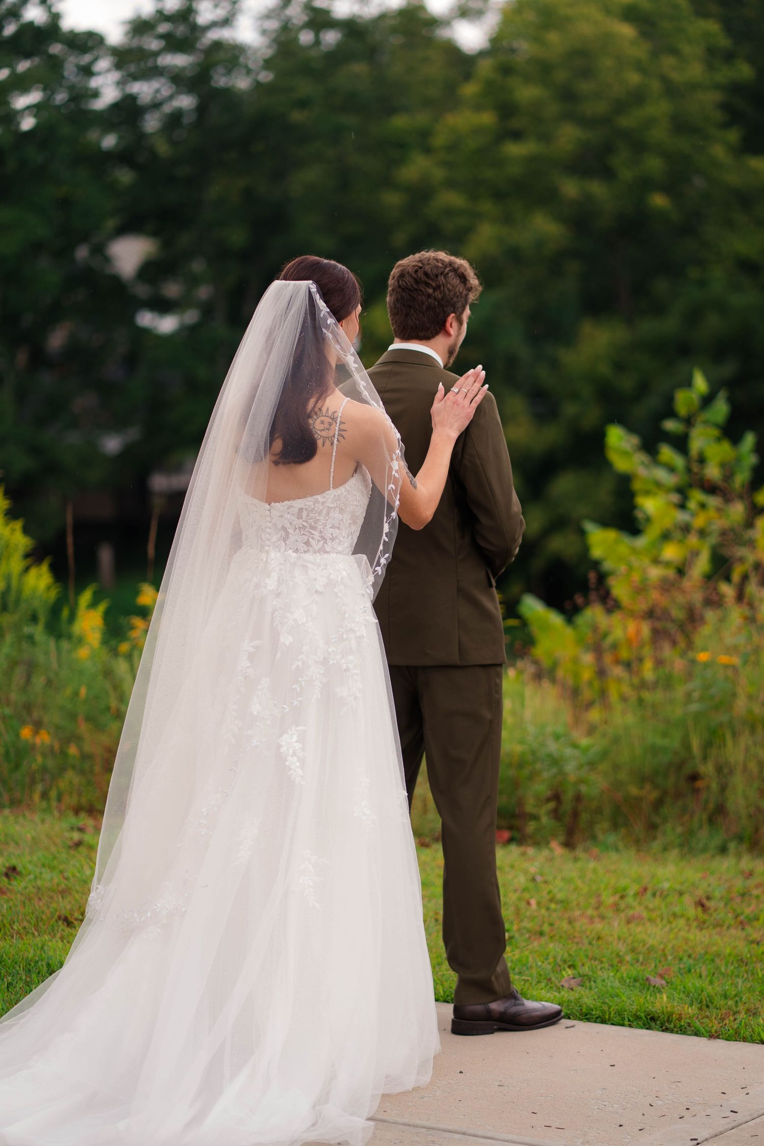 Bride and groom stand together outdoors viewing a lush garden landscape on their wedding day.