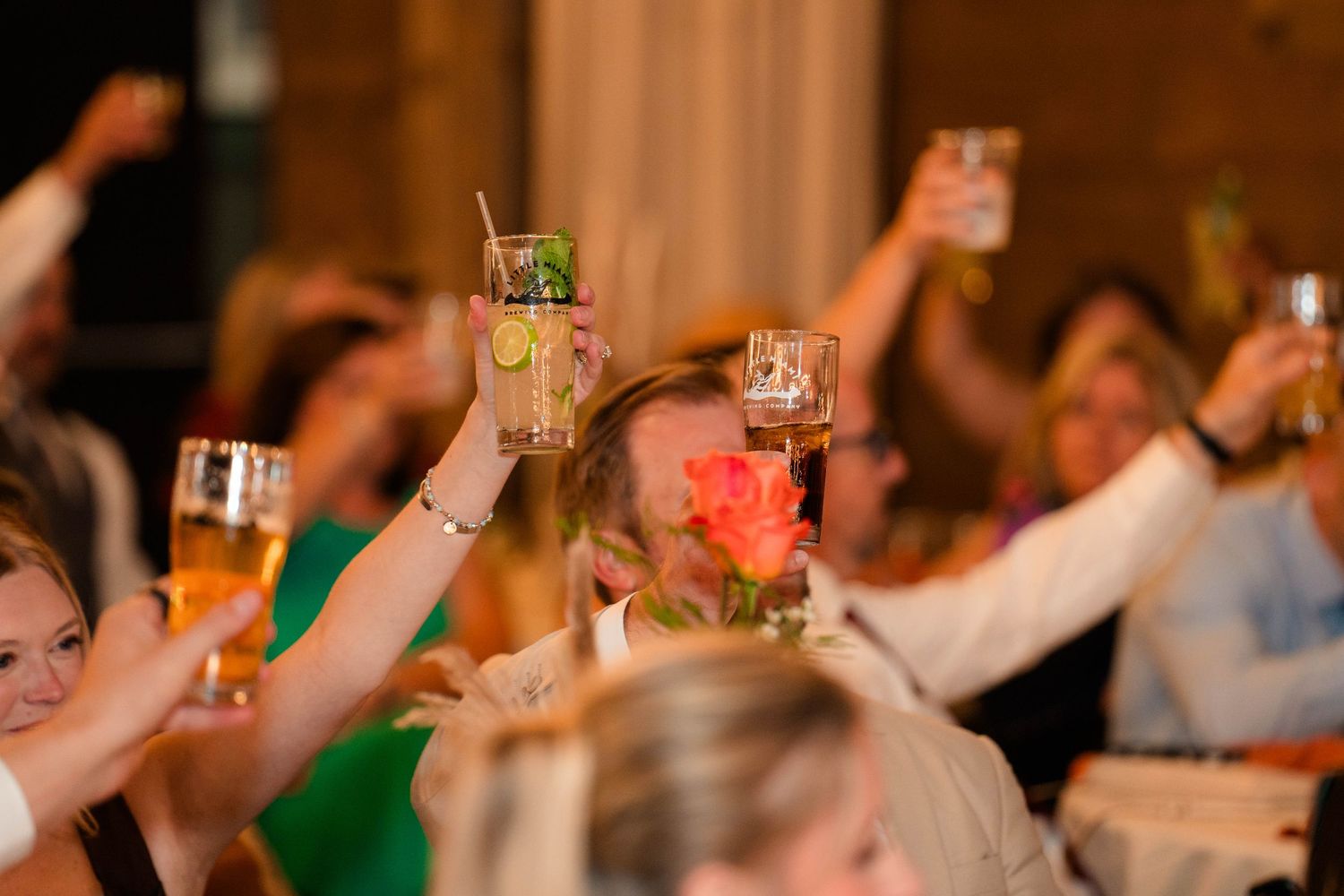 Wedding guests raise glasses in a joyful toast during reception celebration.