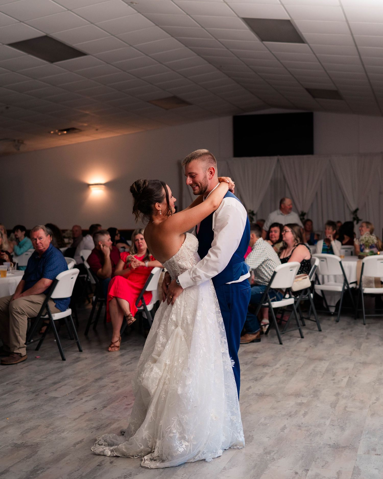 Bride and groom share romantic first dance at wedding reception with guests watching.