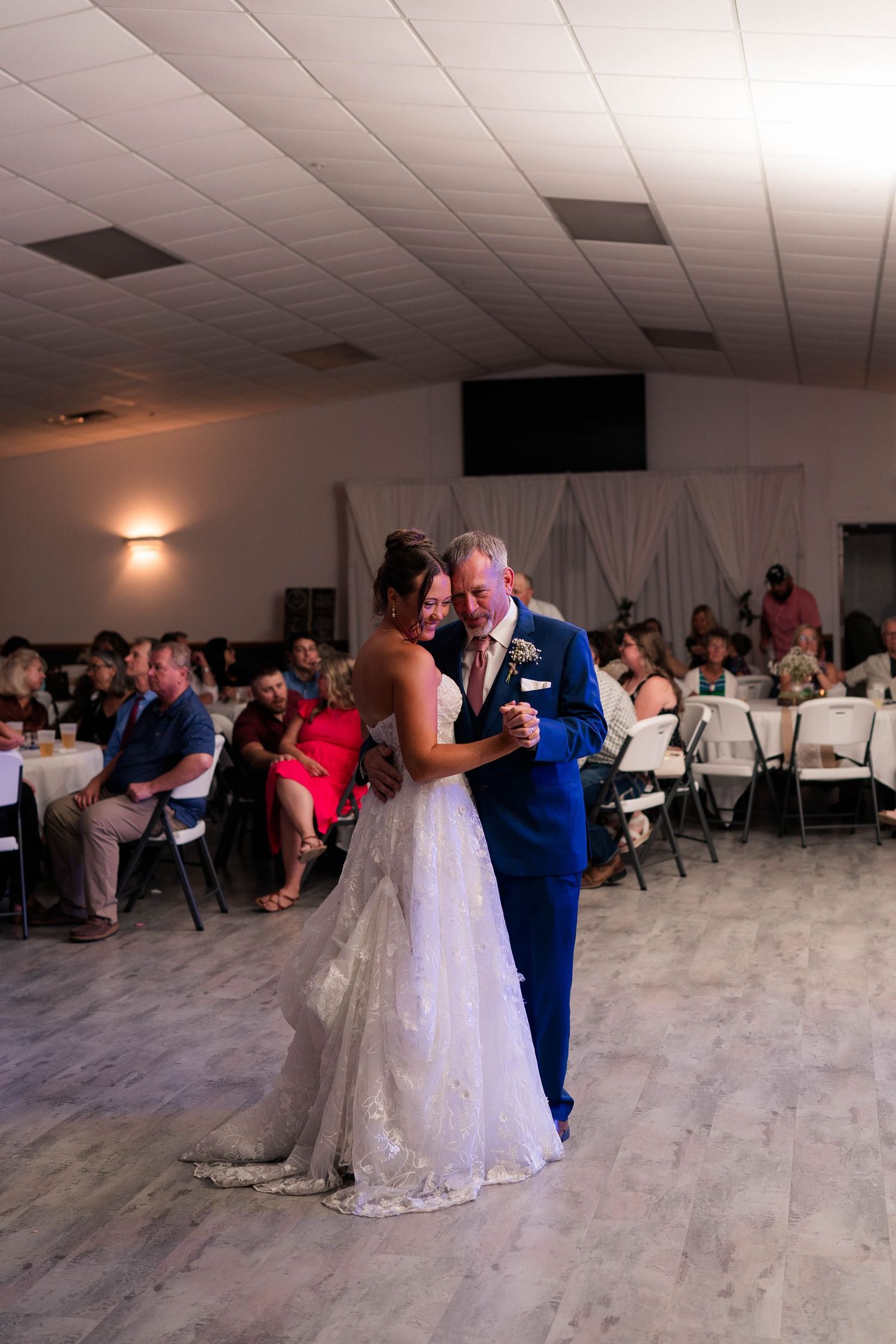 Bride and her father share an emotional dance together at the wedding reception as guests look on.