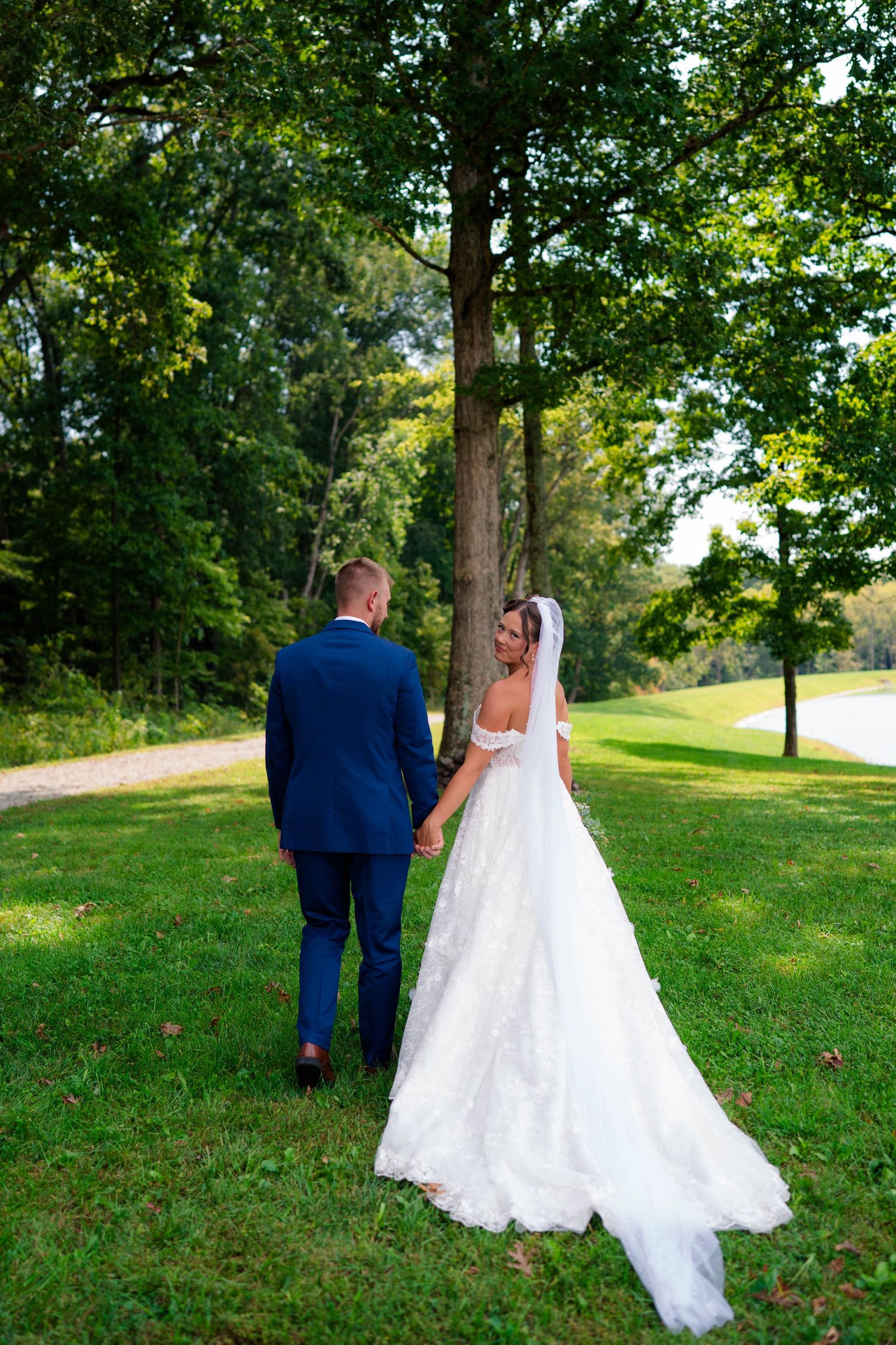 Wedding couple strolling hand in hand near tall trees in a scenic outdoor setting.