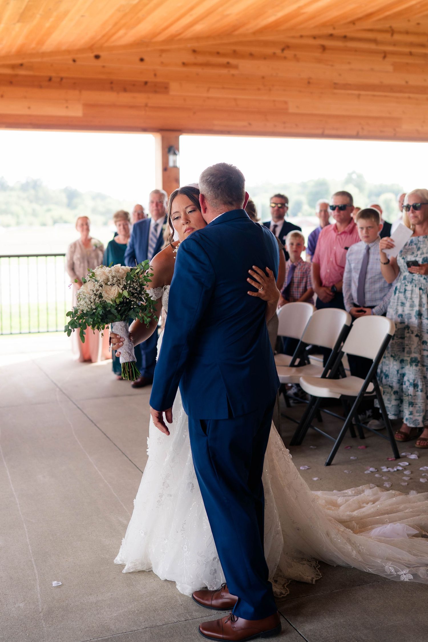 Bride embracing father during emotional wedding ceremony walk down the aisle at outdoor venue.