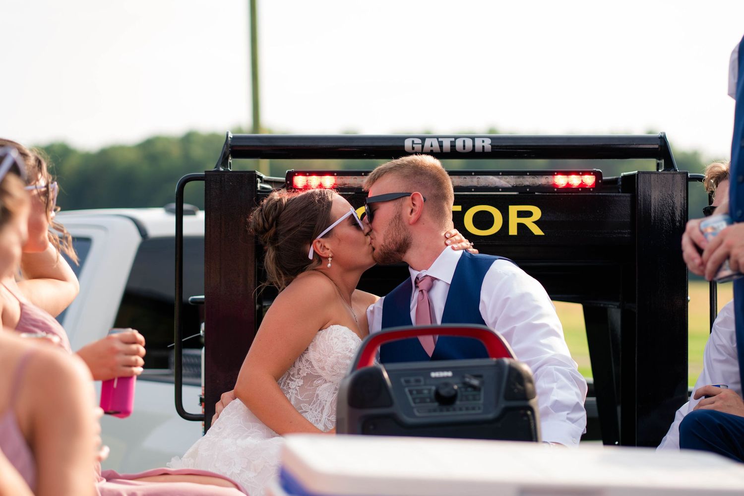 Bride and groom share a kiss while riding in a Gator utility vehicle at their outdoor wedding.