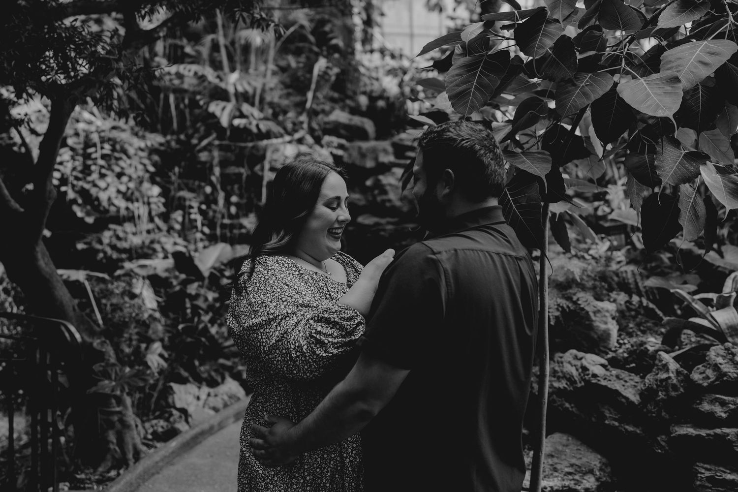 Black and white photo of a couple sharing a tender moment surrounded by tropical foliage.