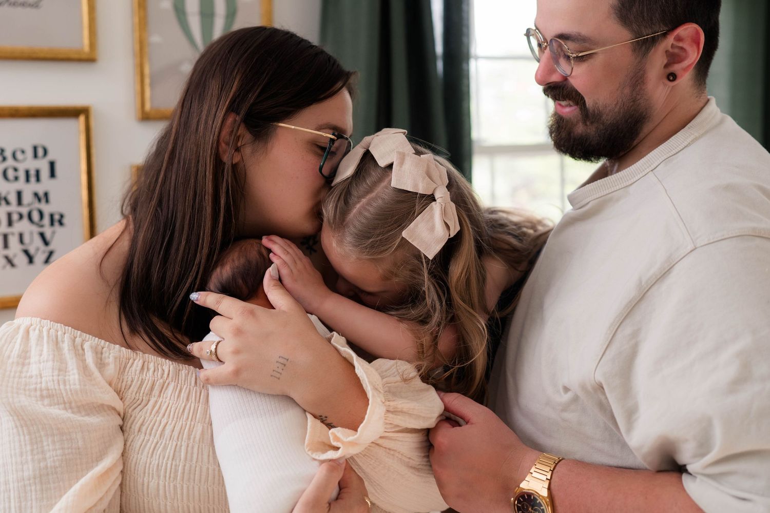 Mother kissing toddler daughter while father watches during newborn photo session.