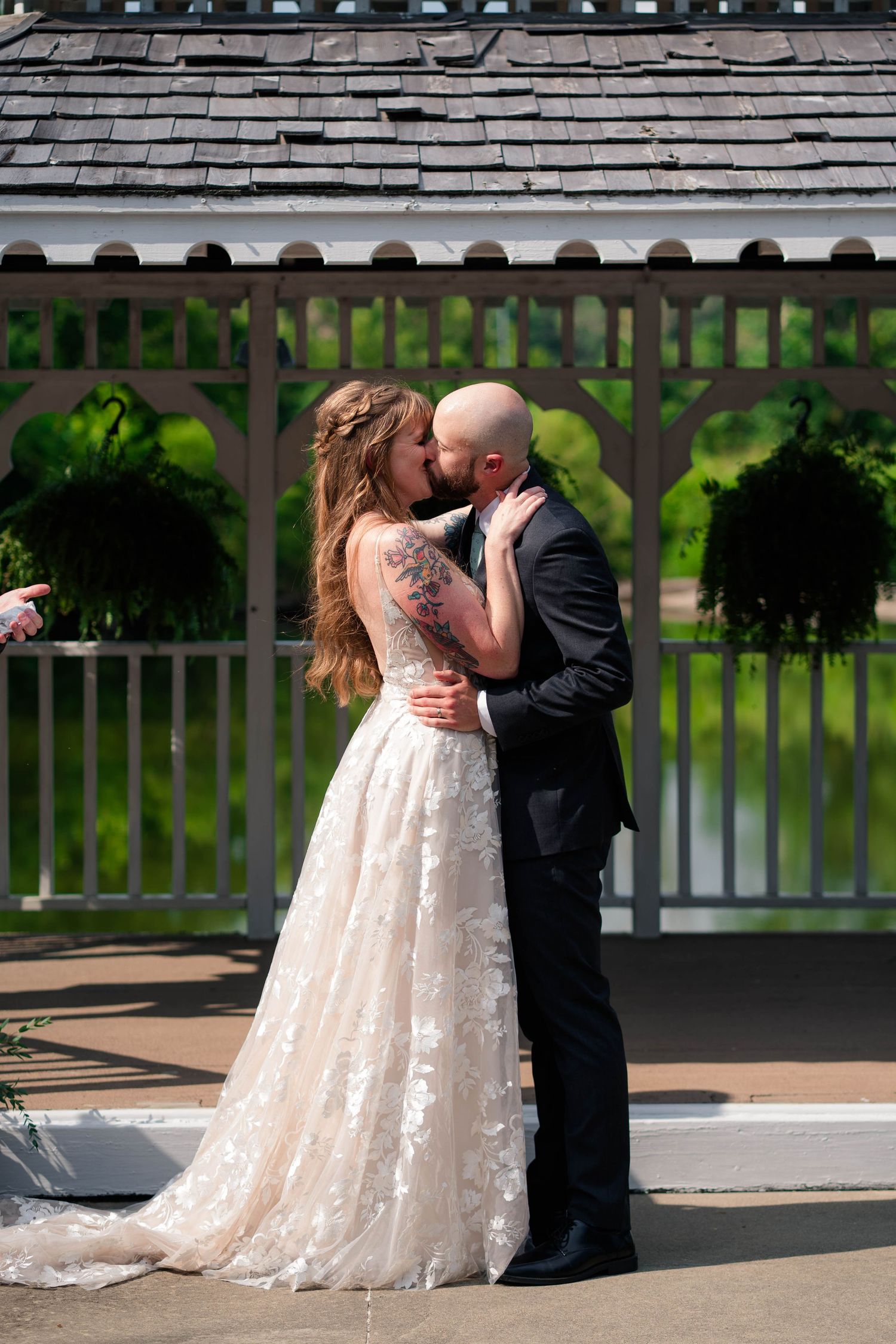 Bride and groom share first kiss in front of white gazebo after outdoor wedding ceremony.