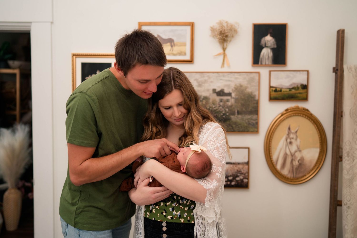 Young couple in green and white outfits lovingly gazing at newborn baby against gallery wall.