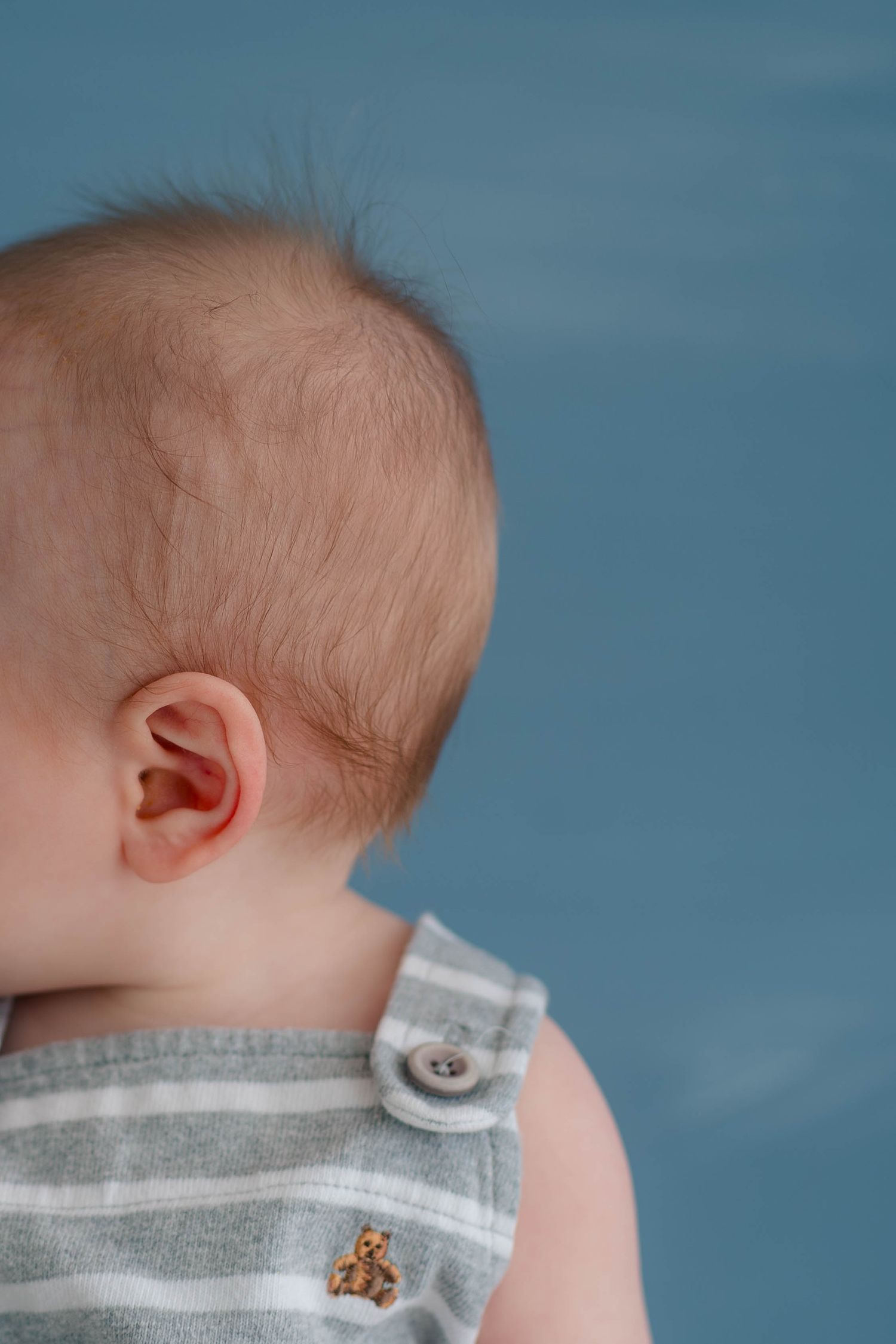 Close-up back view of a baby wearing a gray striped romper with button detail against blue background.