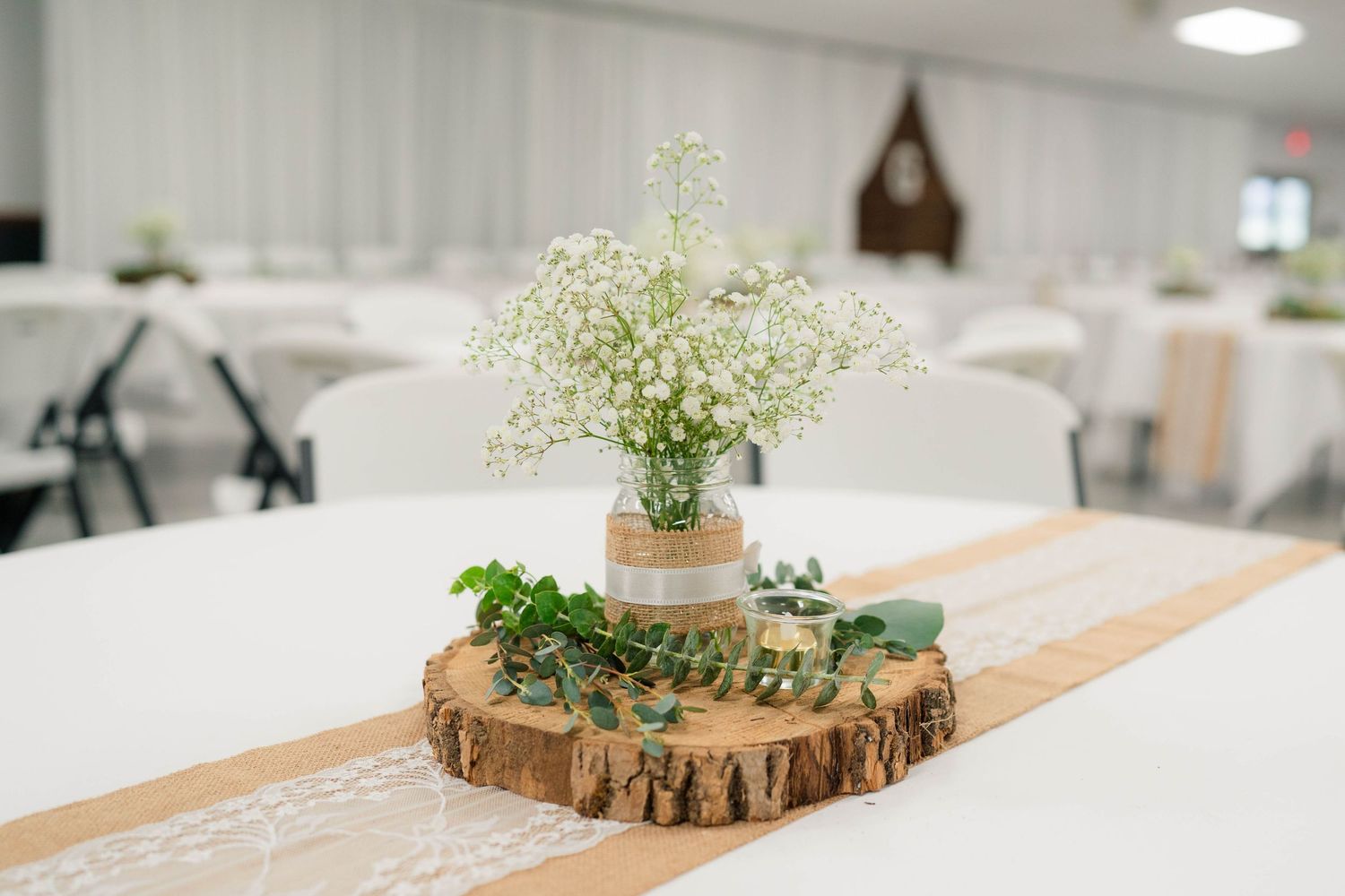 Rustic wedding centerpiece with baby's breath in a mason jar on a wood slice with eucalyptus.
