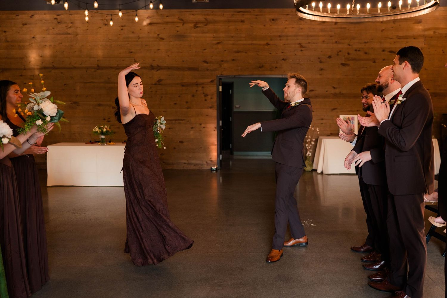 Bridesmaid and groomsman performing energetic dance at wedding reception in rustic venue.