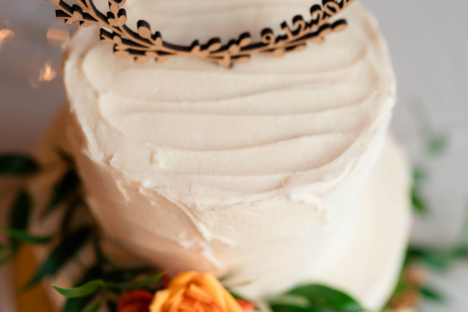 Elegant two-tier white wedding cake with decorative laser-cut topper and colorful floral accents.