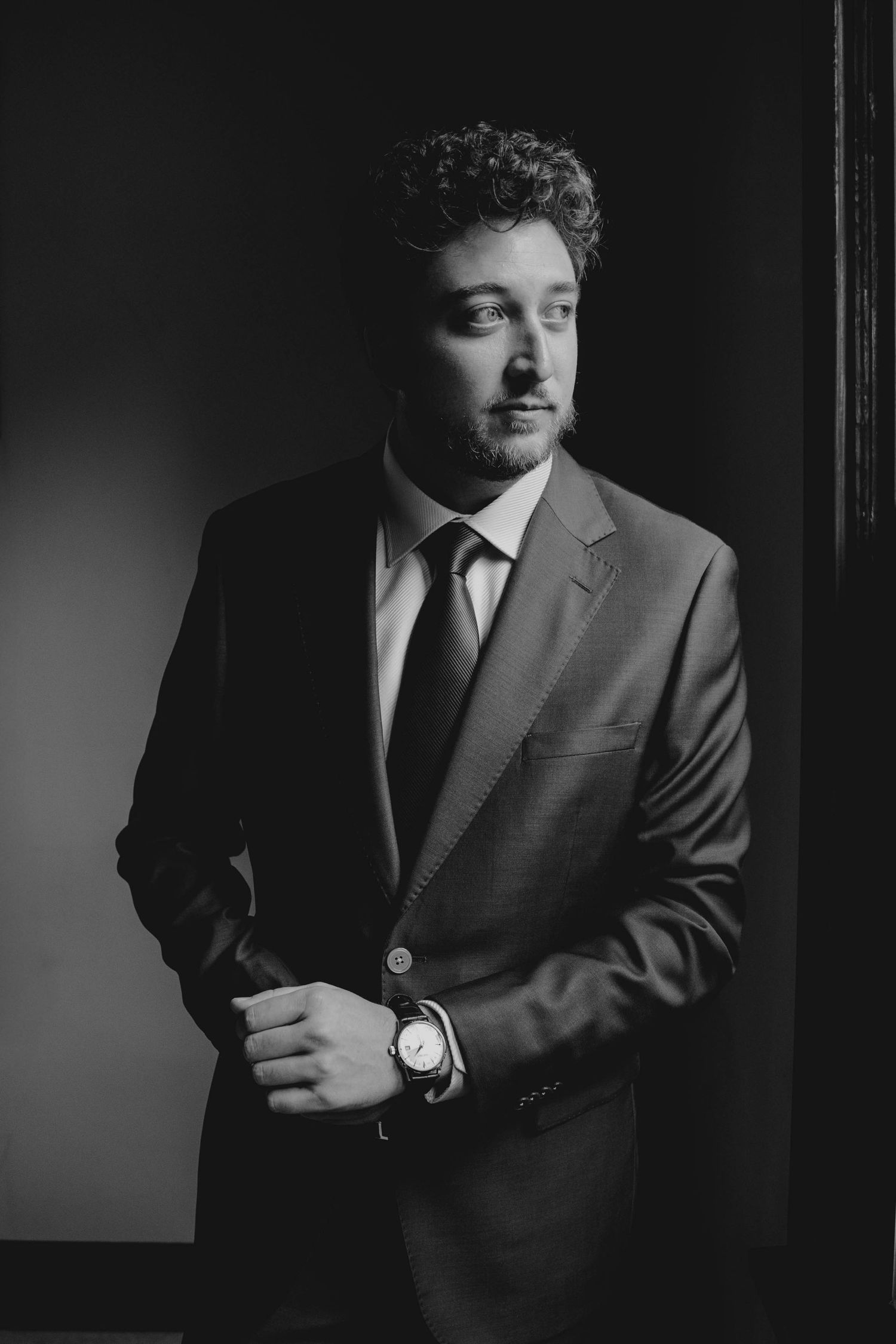 Black and white portrait of a well-dressed man in a suit and tie, adjusting his watch cufflink.