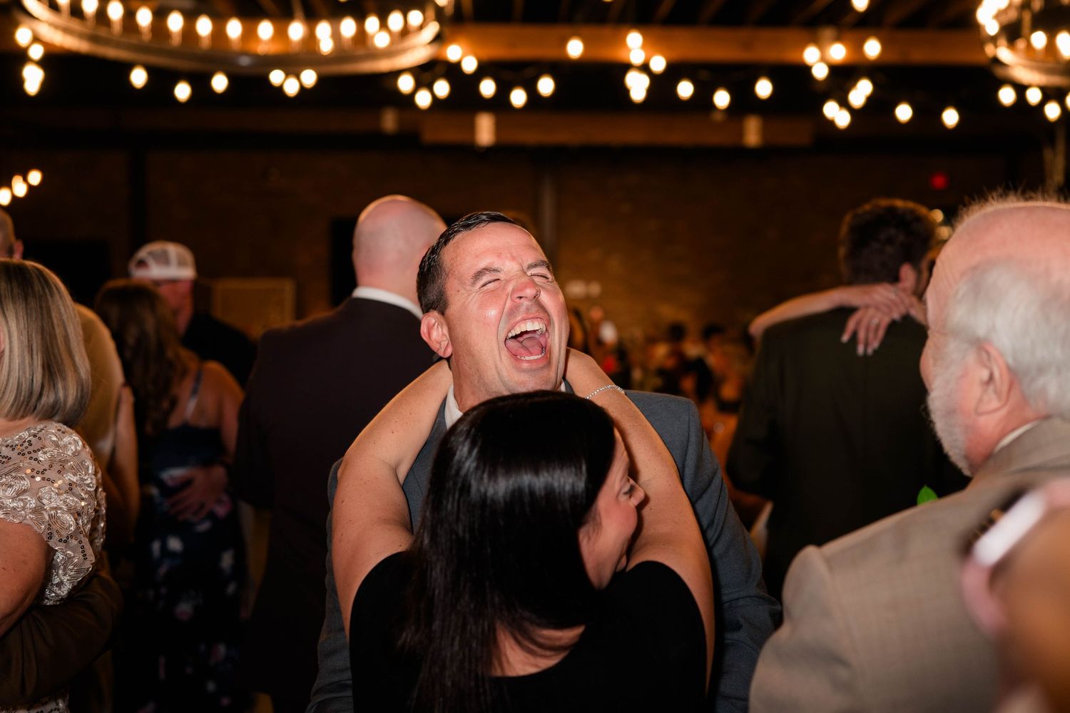 Excited wedding guest laughing and dancing at lively indoor wedding reception.