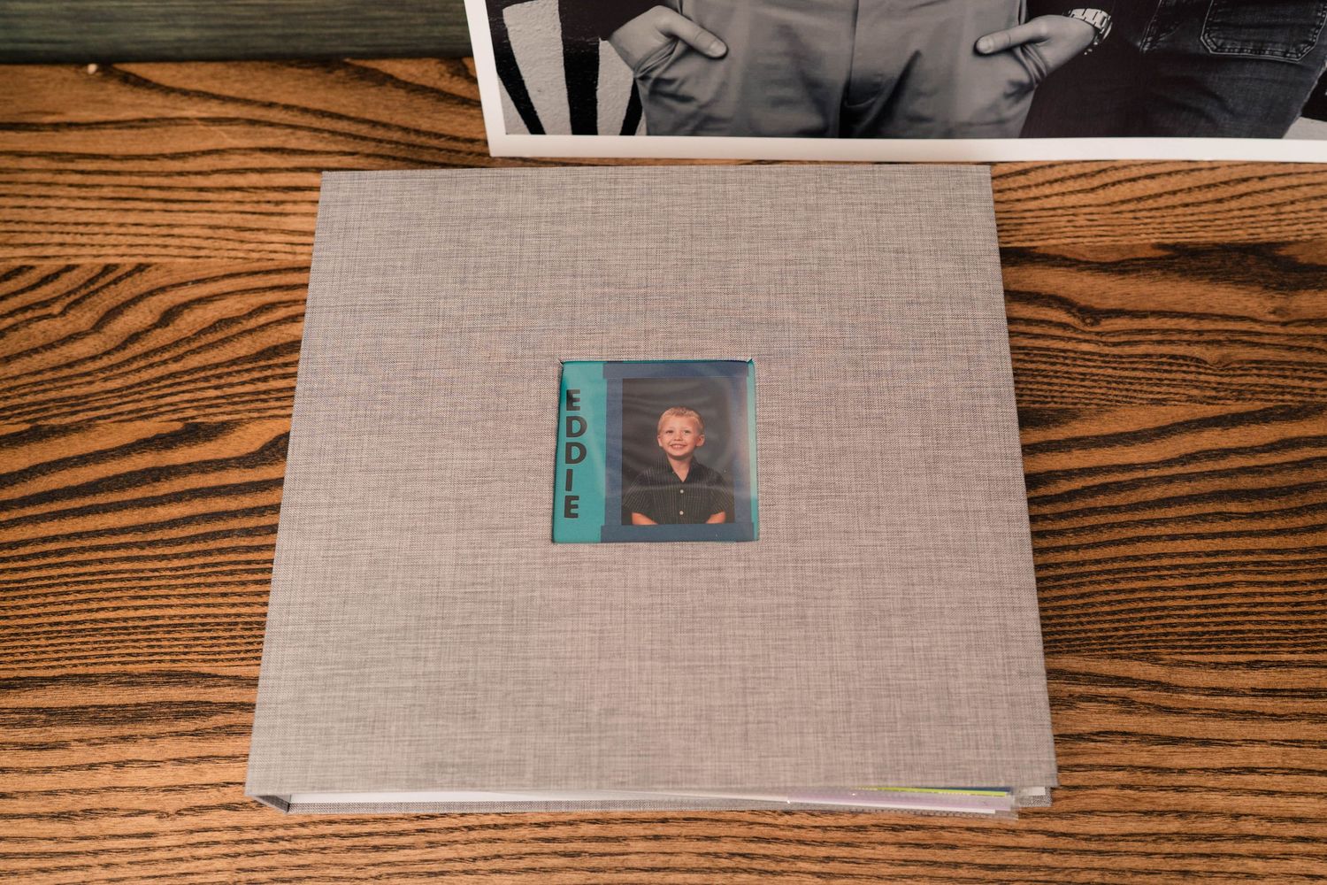 Gray linen-covered photo album with a childhood portrait labeled Eddie displayed on a wooden surface.