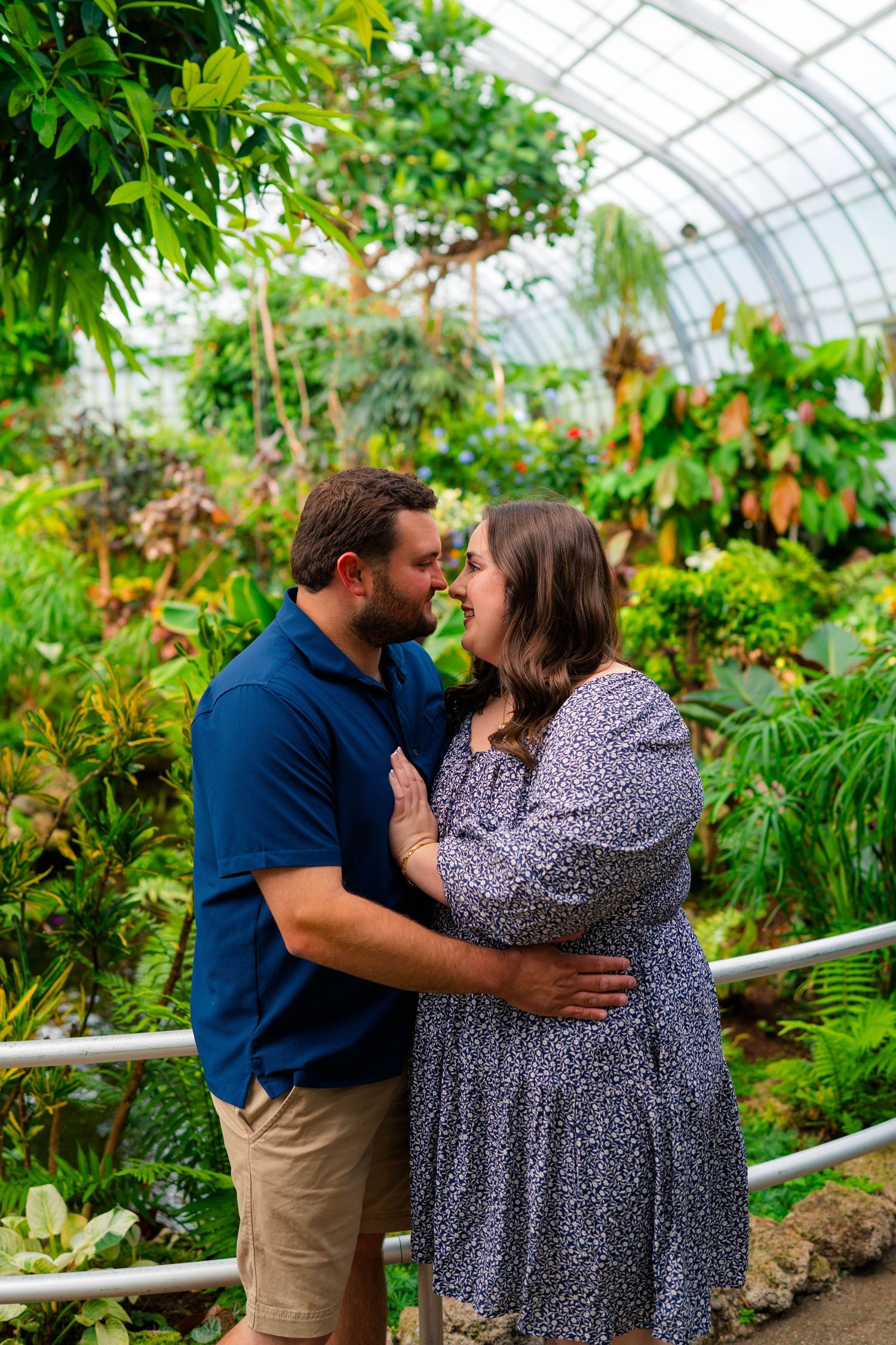 Couple sharing a romantic moment in a lush greenhouse botanical garden, surrounded by tropical plants.