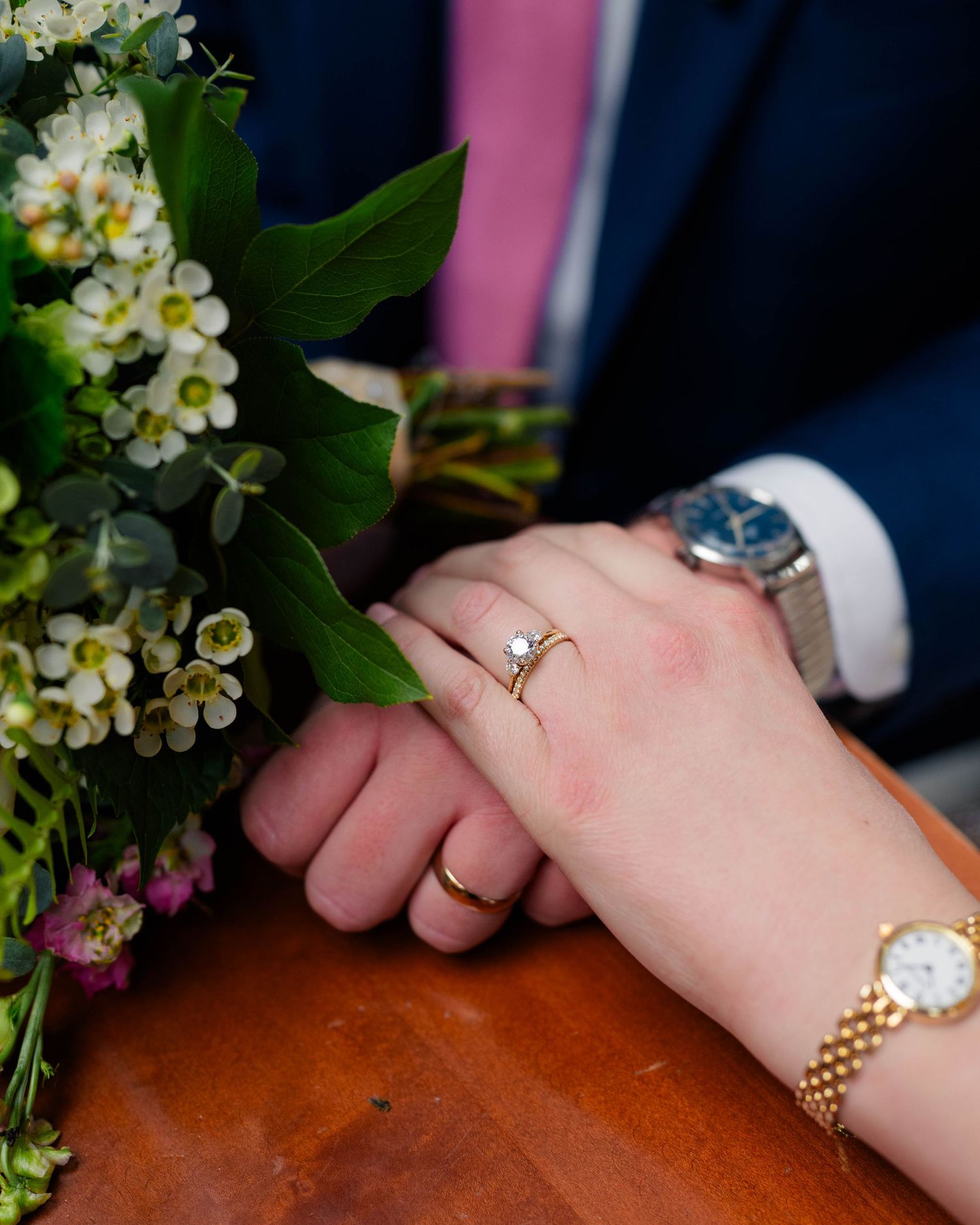 Close-up of bride and grooms hands showing wedding rings beside a white floral bouquet.