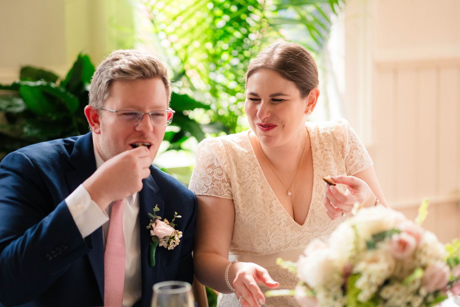 Bride and groom sharing a joyful moment tasting food at their wedding reception sweetheart table.