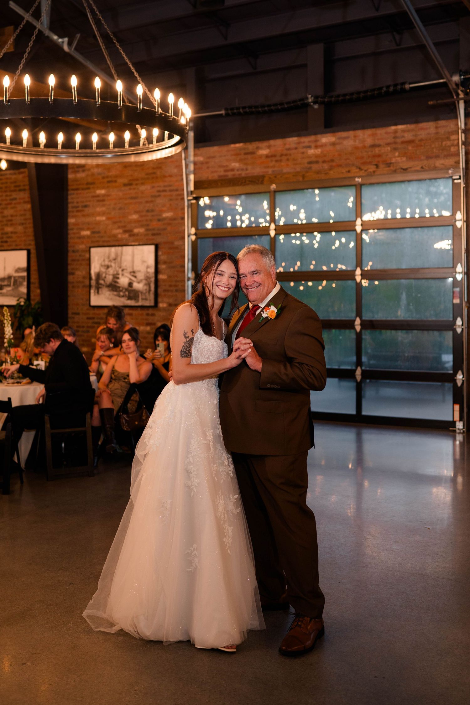 Bride and older gentleman share father-daughter dance under chandelier at elegant wedding reception.