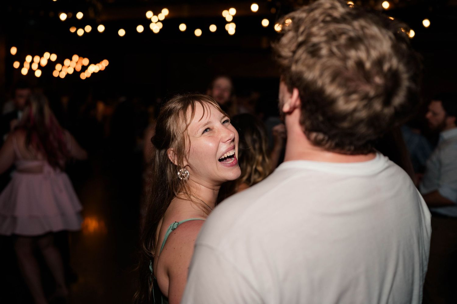 Young woman laughs joyfully while dancing with partner at festive wedding reception.