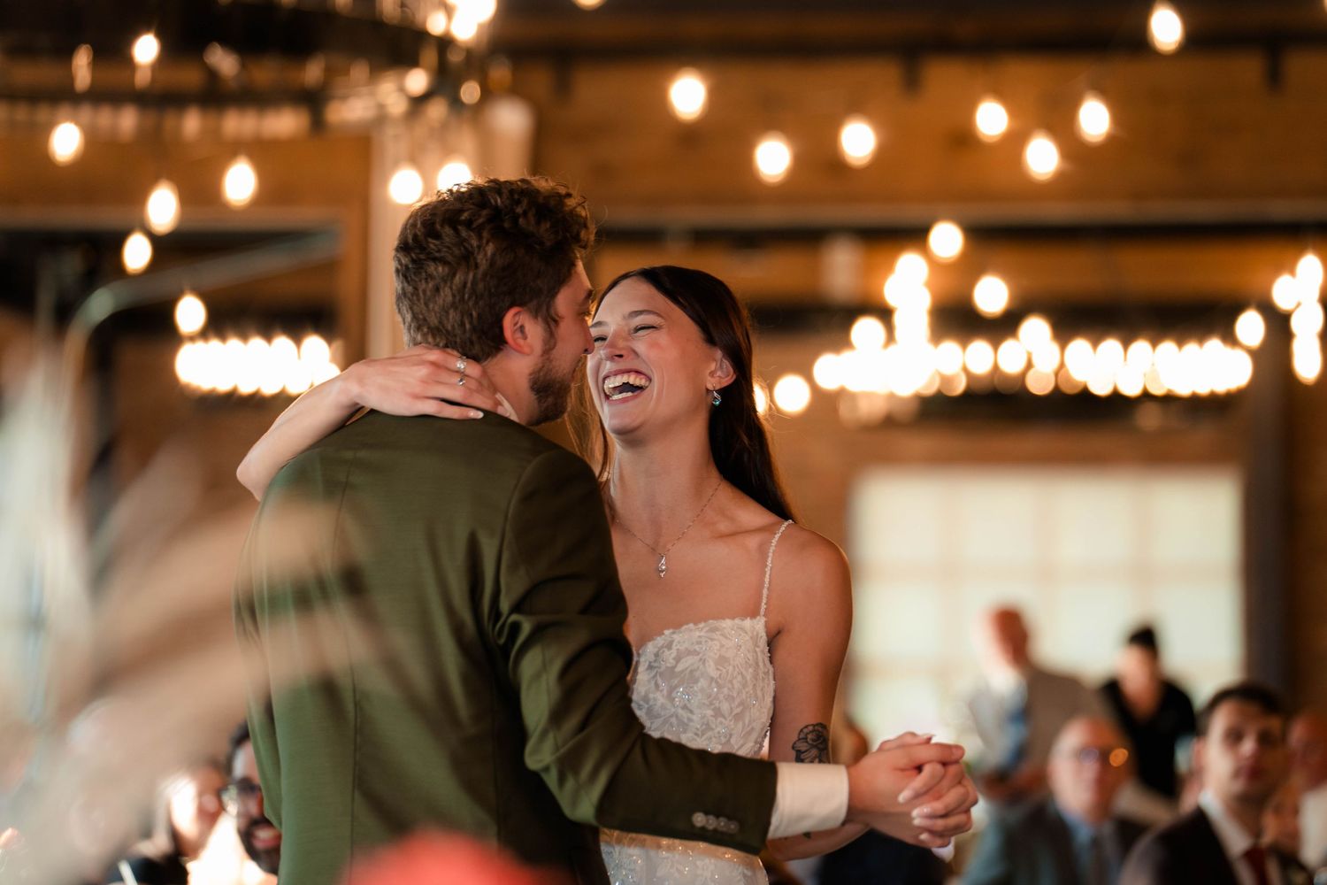 Bride and groom sharing a joyful first dance under warm string lights at their wedding reception.