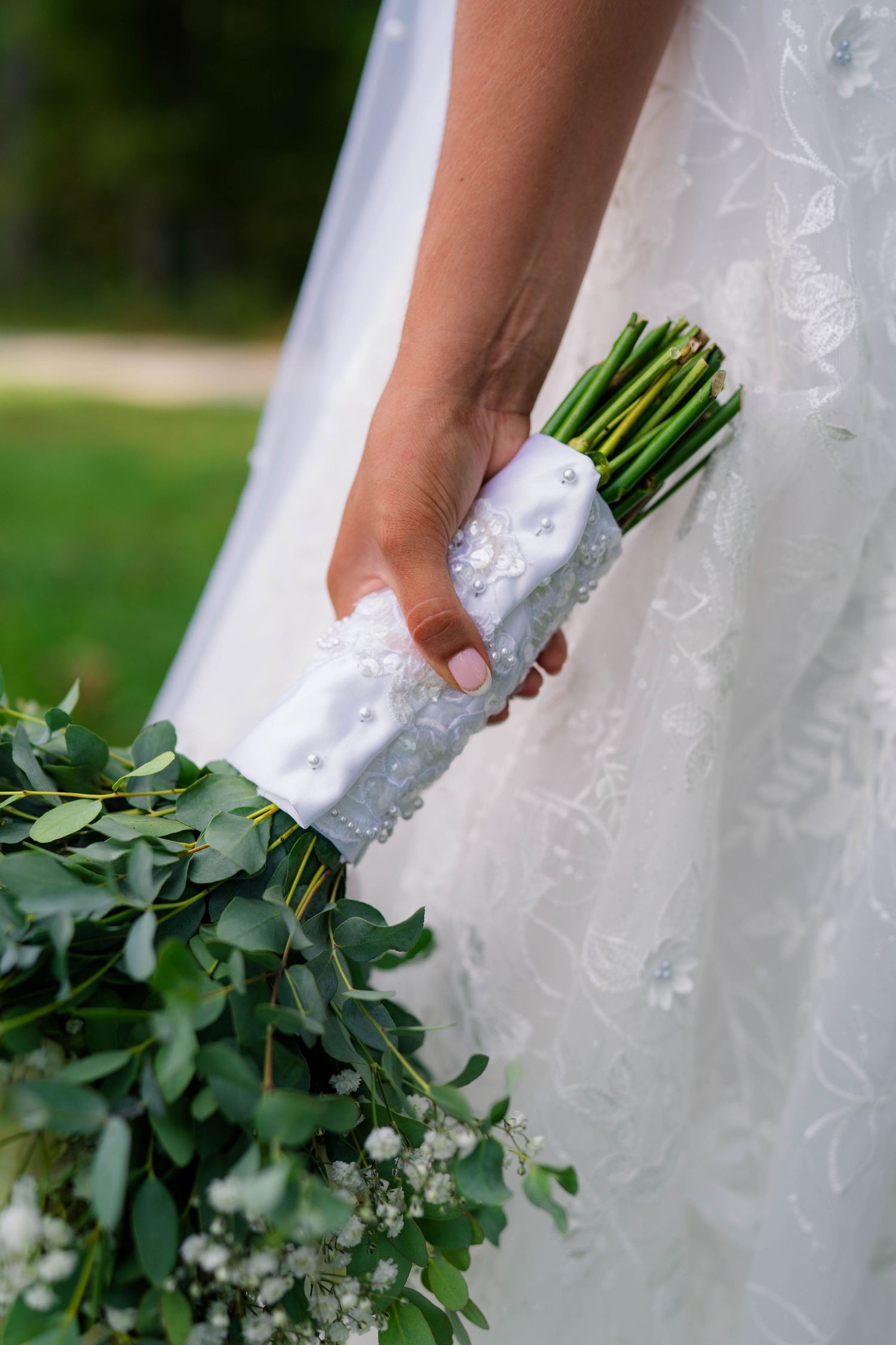 Bride holding a wedding bouquet of eucalyptus and baby's breath with white ribbon wrap.