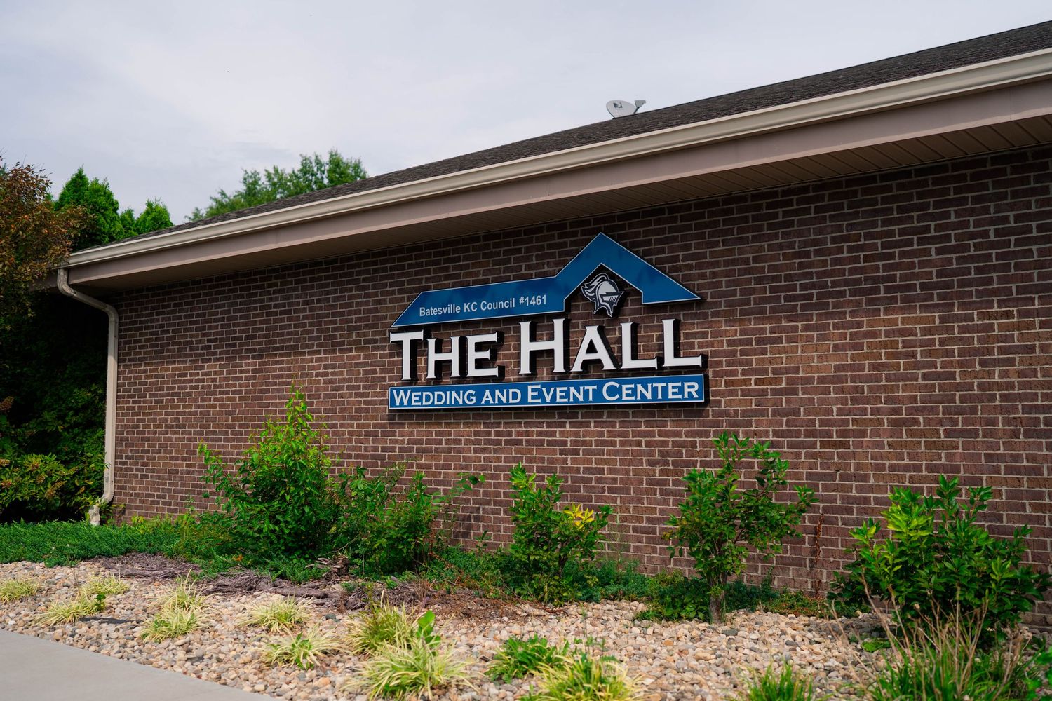 Exterior brick sign for The Hall Wedding and Event Center surrounded by green landscaping.