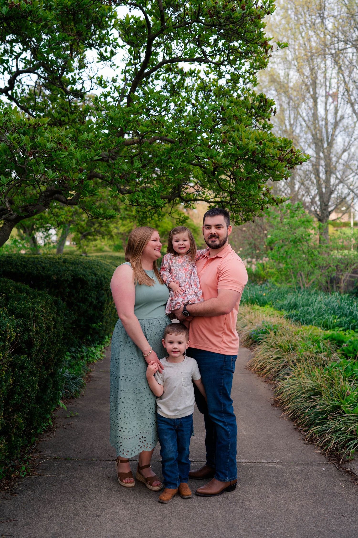 Happy family of four posing on a garden path under a large tree.