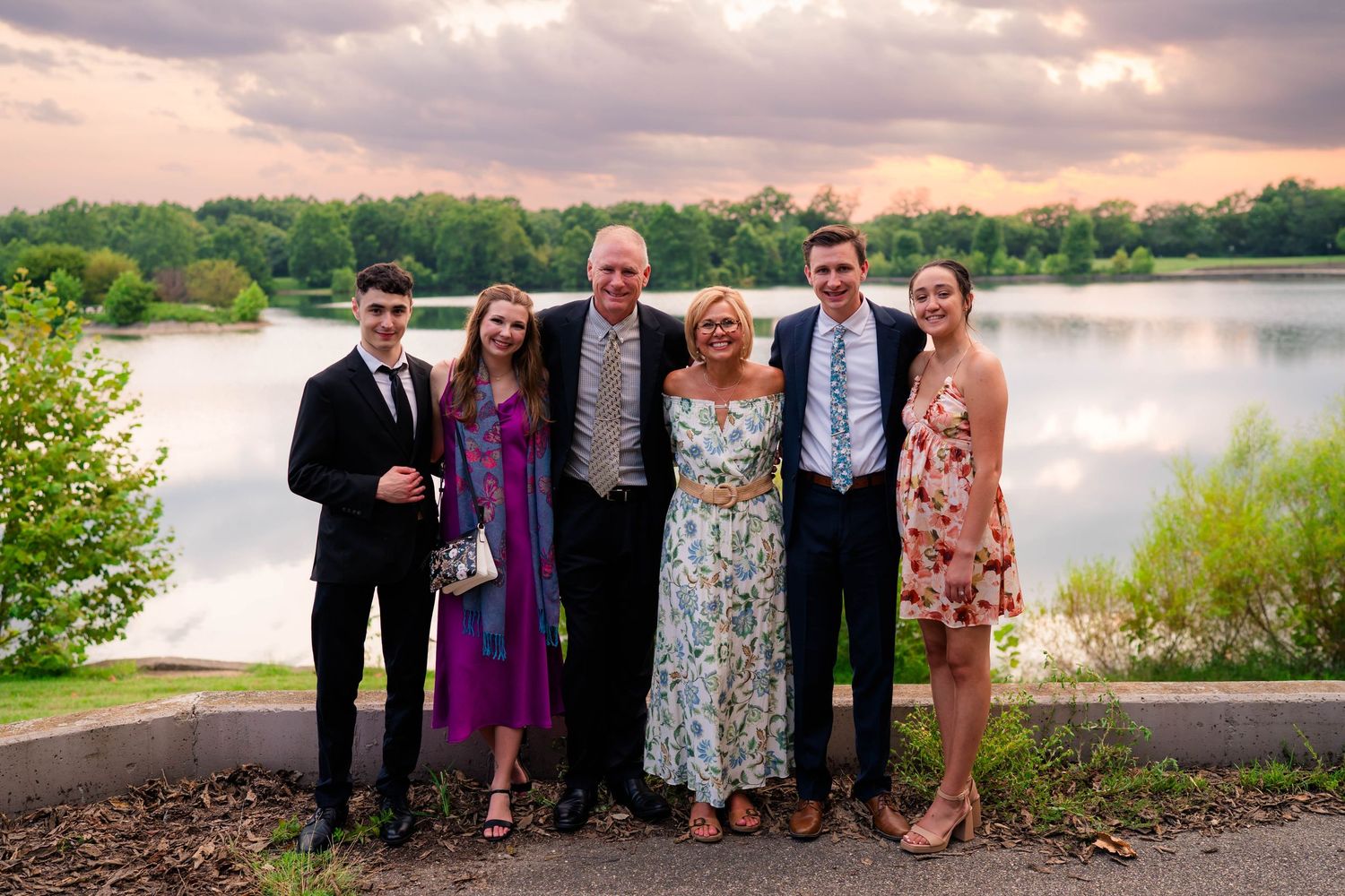 Family of six poses together in formal attire by scenic lake at wedding.
