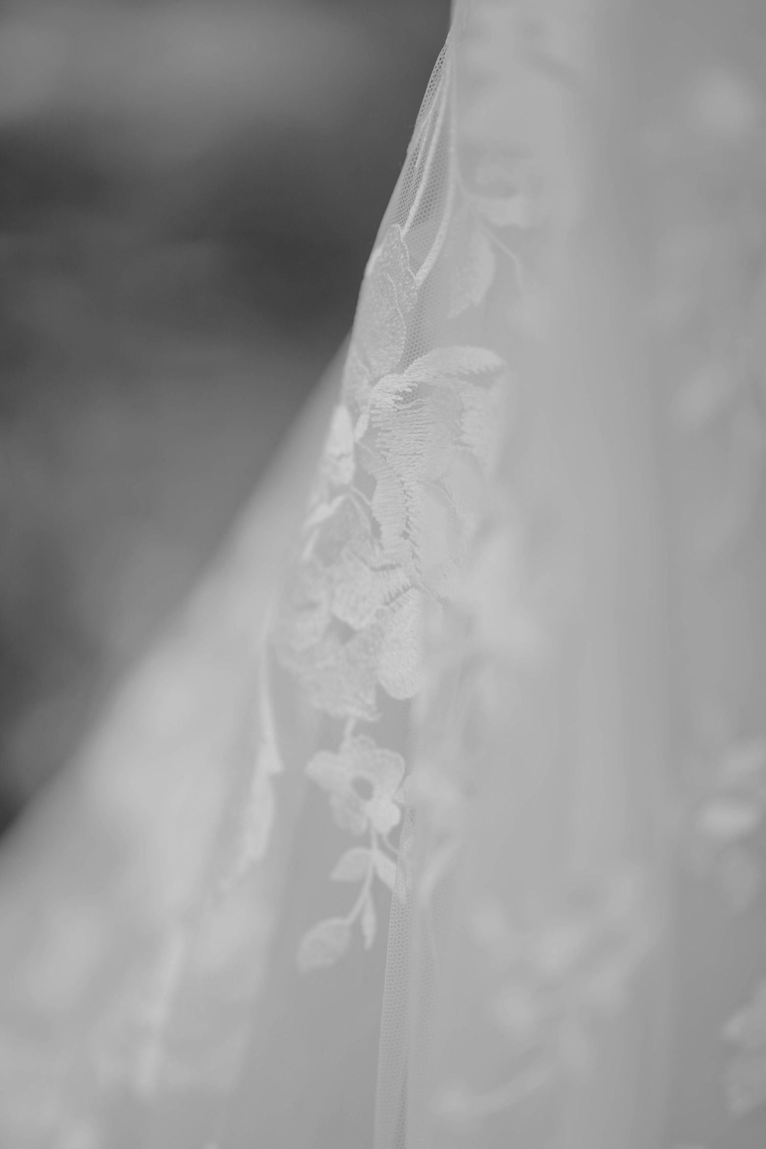 Close-up black and white detail of delicate floral lace embroidery on a bridal wedding gown.