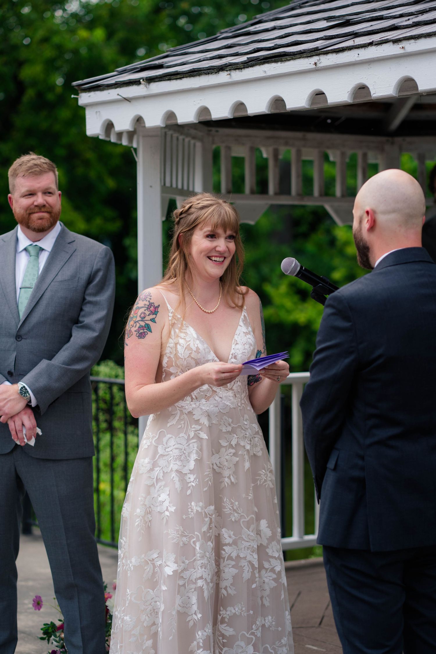 Bride laughs while reading vows at outdoor gazebo wedding ceremony.