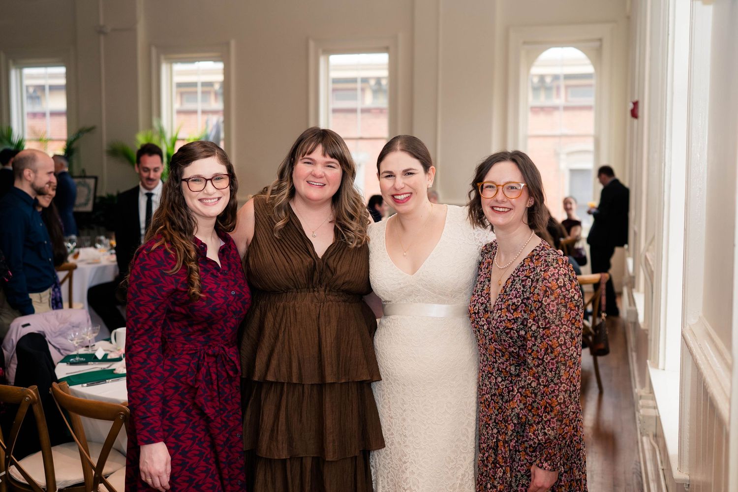 Bride in white lace dress posing with three women at wedding reception.