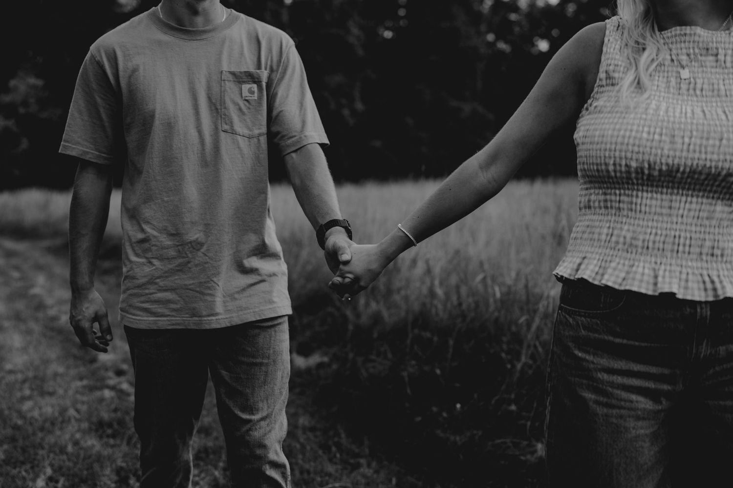 Black and white photo of a couple holding hands while walking through a grassy outdoor path together.