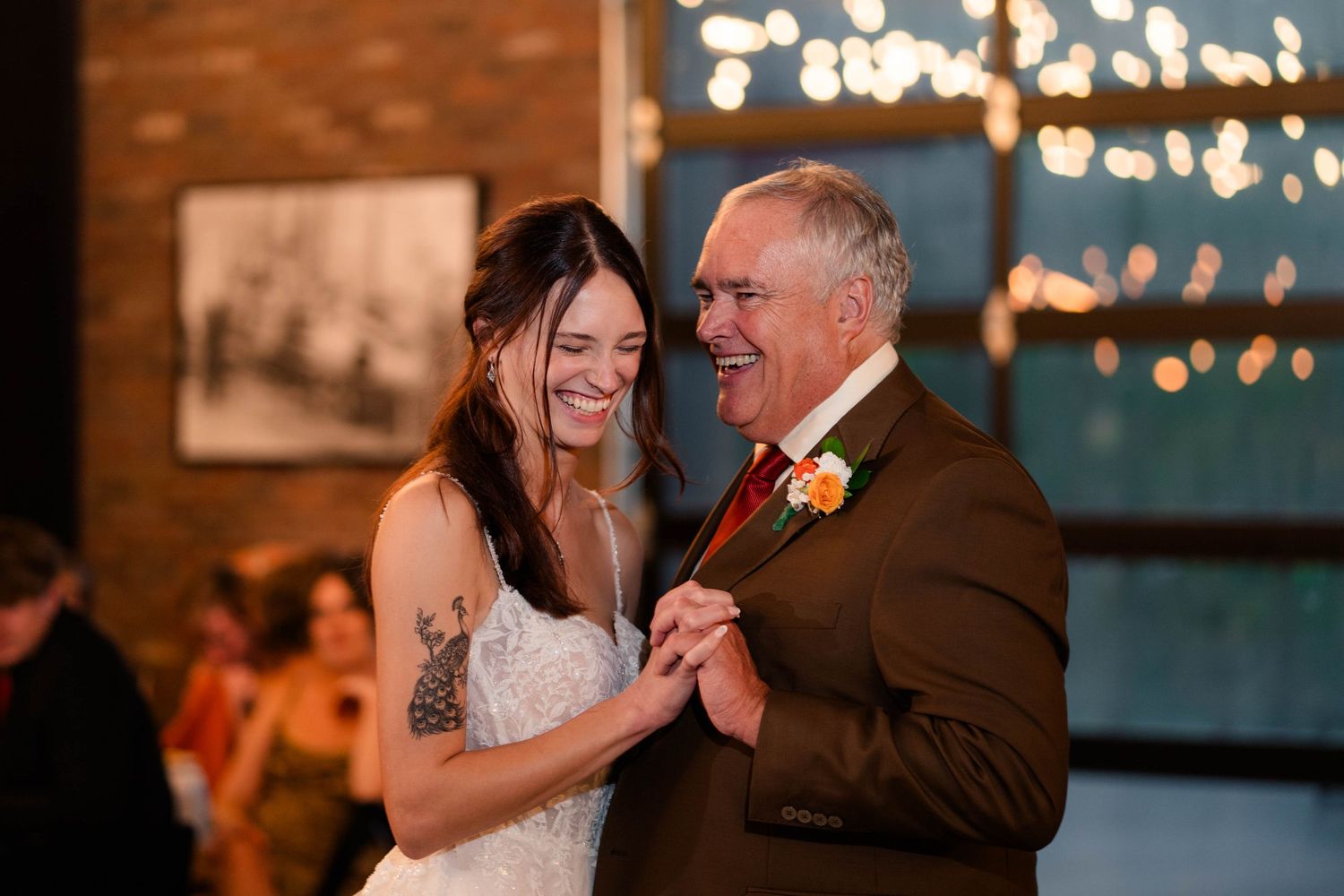 Bride shares a joyful father-daughter dance under warm string lights at wedding reception.