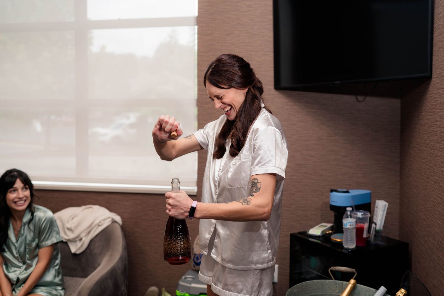 Woman in white uniform smiling while opening a bottle in a brightly lit room.