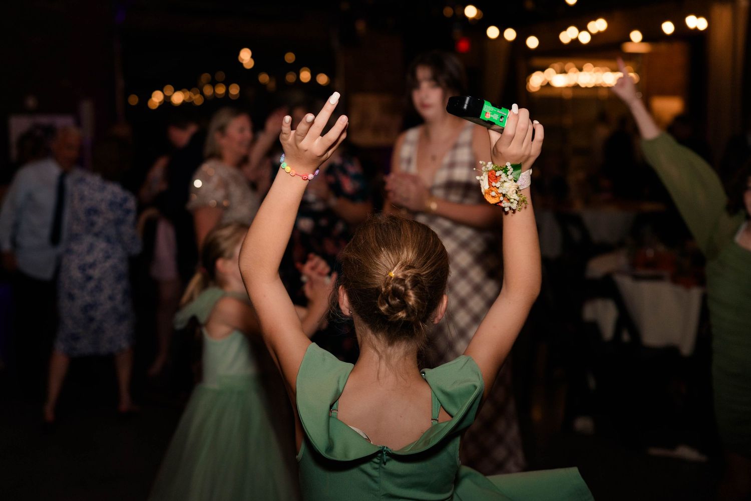 Young flower girl in green dress dancing with hands raised at wedding reception.