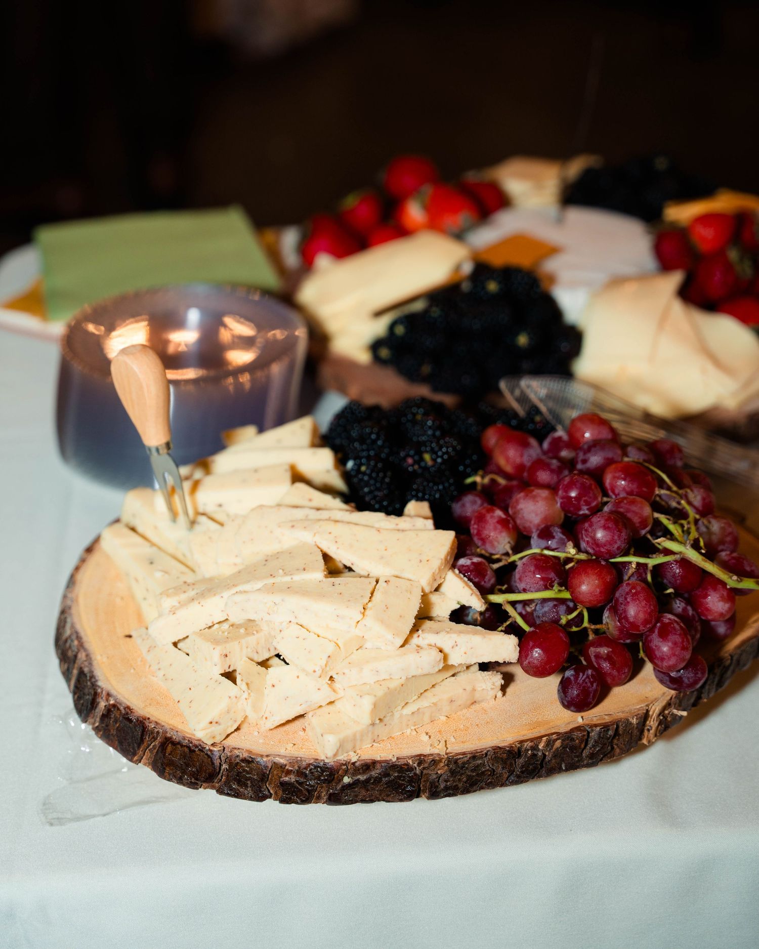 Rustic wood slab charcuterie board with grapes, blackberries, crackers, and cheese at wedding.